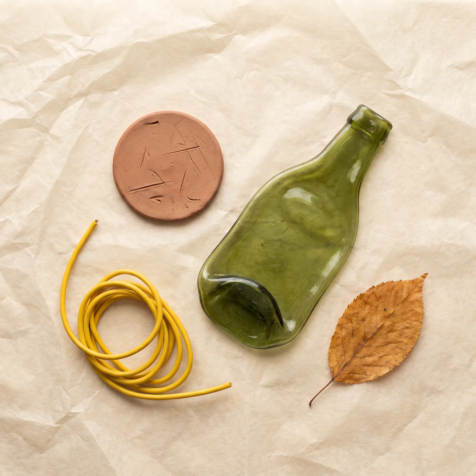 Yellow cord, clay disk and green glass bottle on parchment